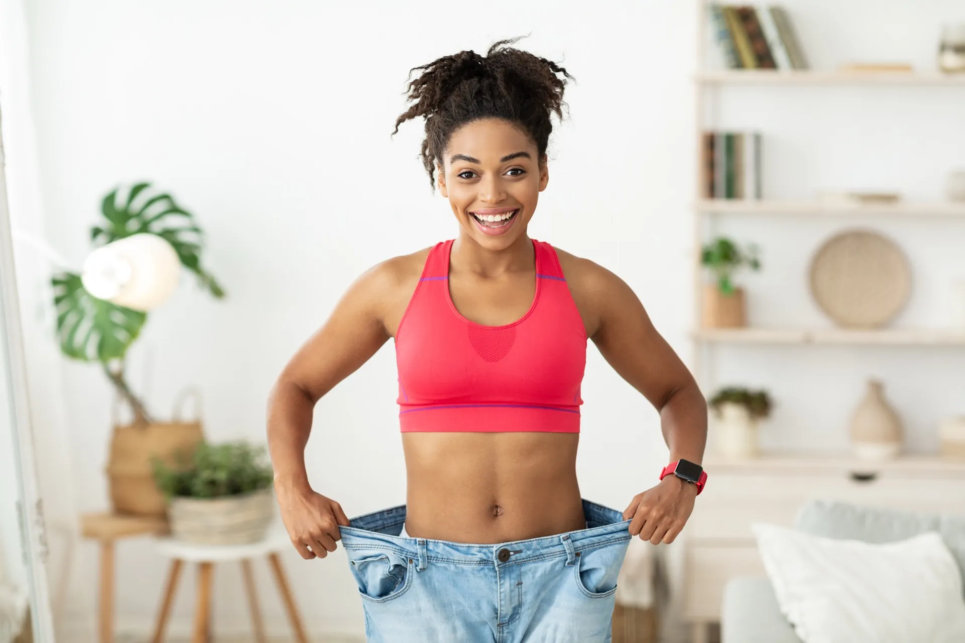 Happy woman with oversized jeans showing weight loss success with retatrutide at Rewind Anti-Aging Miami